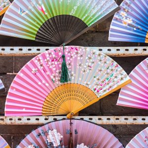 A vibrant display of traditional decorative paper fans featuring intricate floral designs and tassels.